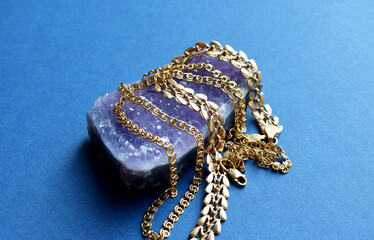 Different gold chains on a purple amethyst druse lie on a blue table. Gold jewelry.