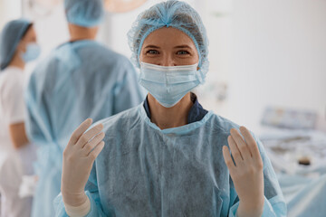 Portrait of female surgeon in mask and gloves standing in operating room, ready to work on patient