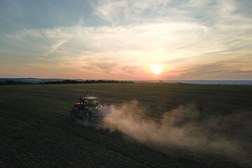 Fototapeta premium Tractor spraying fertilizers with insecticide herbicide chemicals on agricultural field at sunset