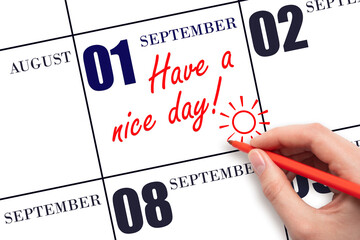 The hand writing the text Have a nice day and drawing the sun on the calendar date September 1