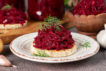 Homemade appetizer of beets, carrots, onions and garlic on toasted bread and in jars on brown table, close-up