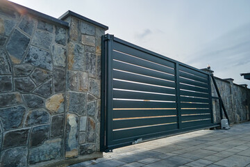 Wide automatic sliding gate with remote control installed in high stone fense wall. Security and...