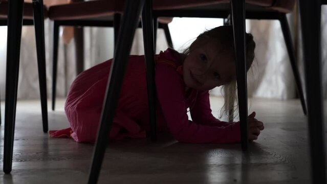 Cute cheerful little girl hides from her mom under table