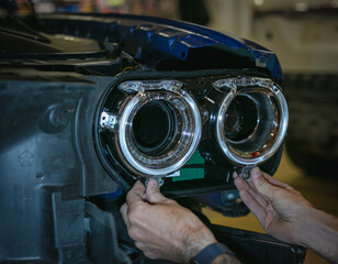 Car headlight in repair close-up. The car mechanic installs the lens in the headlight housing. The concept of a car service.Installation of LED lenses in the headlight. LED lens.Restoration of optics.