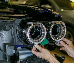 Car headlight in repair close-up. The car mechanic installs the lens in the headlight housing. The...