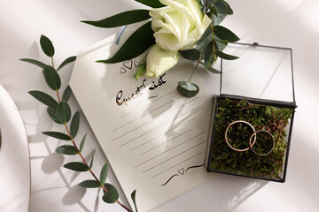Beautiful wedding rings, boutonniere and guest list on white background, top view