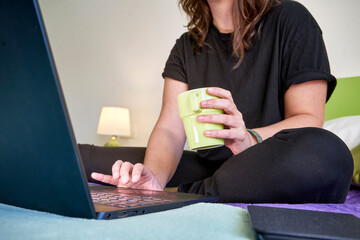 Female working from home by a laptop with a mug in a hand