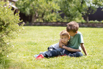 Naklejka na ściany i meble Two little brother boys lie on the grass and hug. Family ties and friendship concept
