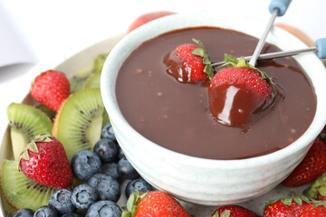 Dipping strawberries into fondue pot with chocolate, closeup