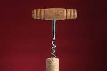 Corkscrew with cork against dark red background, closeup