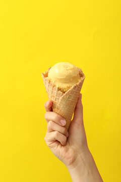 Woman holding waffle cone with delicious ice cream on yellow background, closeup