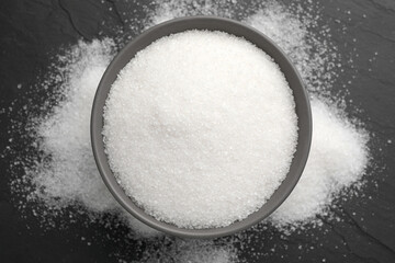 Granulated sugar on black table, top view