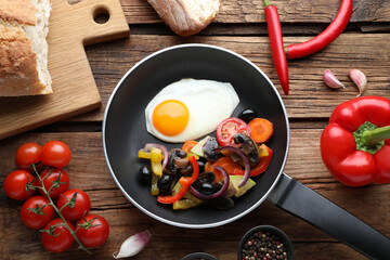 Tasty fried egg with vegetables in pan and ingredients on wooden table, flat lay