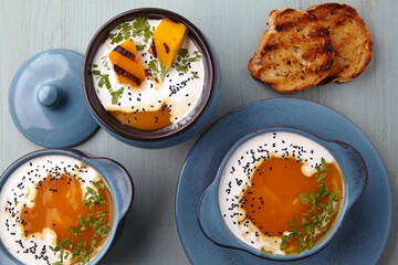 Hot creamy pumpkin puree soup with cream, black cumin seeds, herbs and toasted bread on a blue wooden table. Holiday dinner