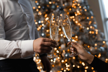 hands of a man and a woman with glasses of champagne against the background of the lights of garlands