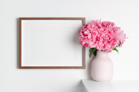 Landscape wooden frame mockup on white wall with fresh pink peony flowers
