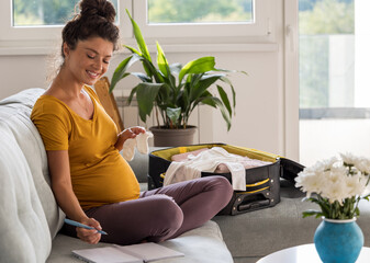 Pregnant woman making checklist for labor and packing suitcase