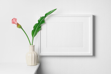 Landscape picture frame mockup on white wall with fresh calla flower