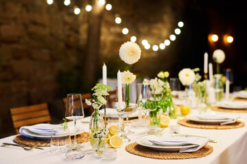 Festive table with two rows of plates with napkins surrounding candles, flowers in vases and wineglasses prepared for wedding feast