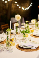Part of served table prepared for wedding party decorated with candles and white dahlia flowers standing between two rows of plates