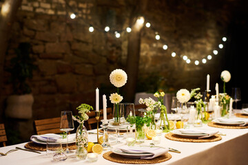 Served dinner table with plates, napkins, wineglasses, flowers and candles prepared for wedding feast in luxurious restaurant or cafe