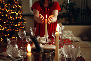 Christmas table, a girl in a red dress holding a candle. Hands and burning candle close-up. Christmas table setting.