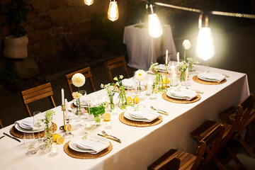 Several bright lamps hanging over festive table served for wedding guests and illuminating objects standing on white tablecloth