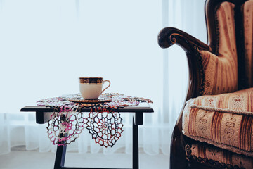 turkish coffee and lace doily under coffee, vintage style armchair wooden, curtain behind them near...