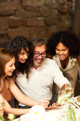 Happy mature man laughing at photos in smartphone taken by one of brides scrolling through new images at wedding party