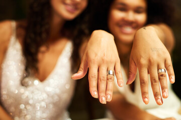 Hands of two young intercultural gay girls showing their wedding rings after getting married while...