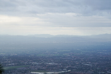 Top view of mountain in Chiang Mai City, Thailand. White cloud and dust is above of the mountain while cities can be seen far away.