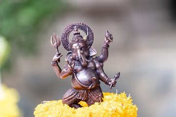 Small replica of Ganesh with iron color is worshiped with a glowing yellow marigold.