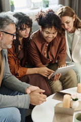 Mature couple and their daughter with her girlfriend gathered in living room for choosing nice wedding gown in online shop