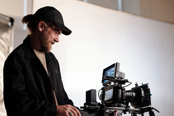 Side view portrait of bearded cameraman watching at screen of steadicam while adjusting focus and...