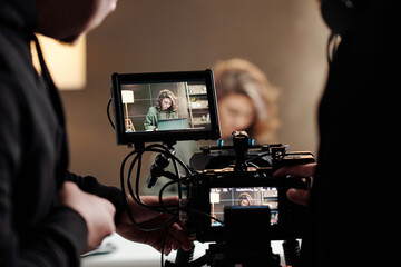 Close-up of steadicam screens with female model using laptop by table during commercial being shot by cameraman and his assistant - obrazy, fototapety, plakaty