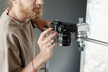 Hand of young modern cameraman adjusting settings of steadicam and fixing it on metallic slider...