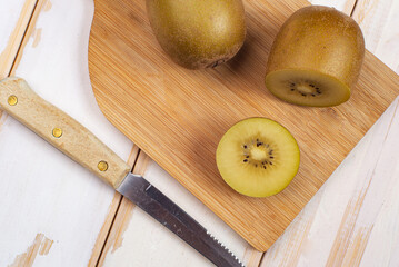 Kiwi sliced and whole fruits on cutting board with knife. On the white table.