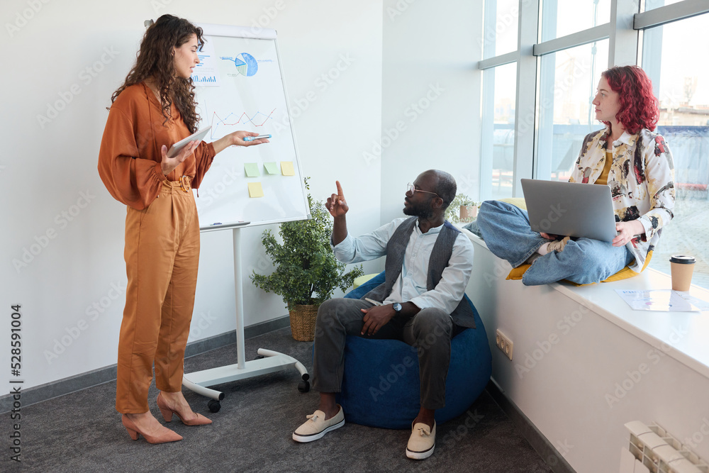 Aufkleber three young intercultural economists discussing financial data on whiteboard while one of them stand