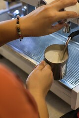 hand of barista working in small cafe using espresso machine to prepare milk frothing for hot coffee