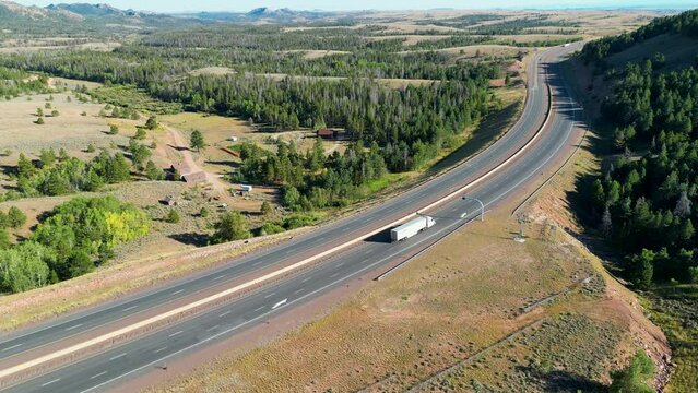 Interstate 80 highway roadway with semis and cars commuting and driving through green rural Wyoming during bright sunny Summer day on 4 lane road from 4k aerial drone video