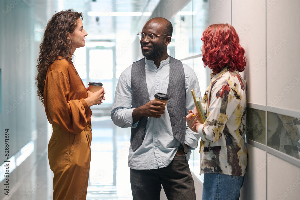 Poster three young successful office managers in casualwear having chat while standing between two walls in