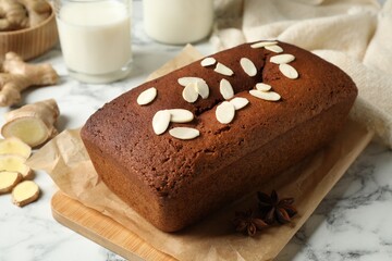 Delicious gingerbread cake with almond petals on white marble table