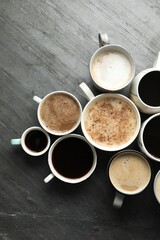 Many cups of different coffees on slate table, flat lay