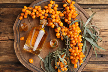 Natural sea buckthorn oil and fresh berries on wooden table, top view