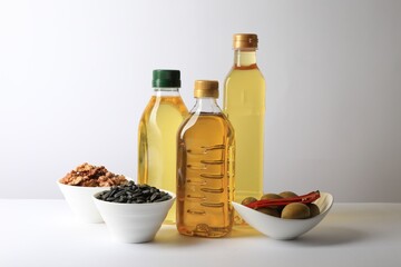 Bottles of different cooking oils, sunflower seeds, walnuts and olives on white background