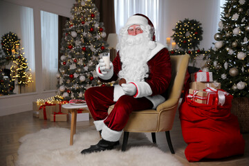 Santa Claus with glass of milk and cookie in room decorated for Christmas