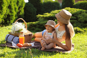 Mother with her baby daughter having picnic in garden on sunny day