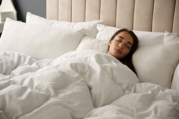 Beautiful young woman wrapped with soft blanket sleeping in bed at home