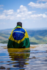 Man with Brazilian flag looking at the horizon. Top of Janela do Ceu Waterfall in Parque Estadual do Ibitipoca (Ibitipoca State Park), Minas Gerais, Brazil