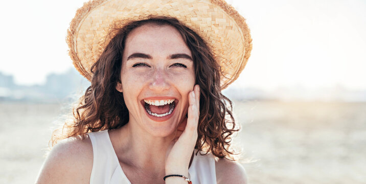 Beautiful young woman with hat smiling at camera outdoors at sunset - Happy female portrait outside